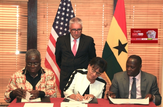 Mr Emmanuel Armah-Kofi Buah (right) and Ms Penny Pritzker signing the MoUs. Those with them are the US Ambassador to Ghana, Mr Gene A. Cretz (standing), and another official. 